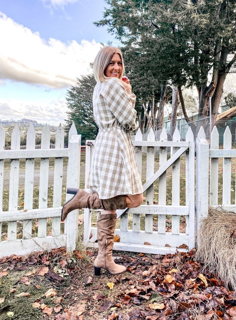 Woman posing in boots & dress next to a white picket fence | StyleFast